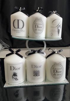 six candles are on a glass shelf with black ribbon around the top and one candle has a monogrammed dior logo on it