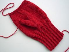 a red knitted mitt sitting on top of a white table next to a pair of scissors