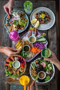 several people are eating food from bowls and plates on a wooden table with two orange juices