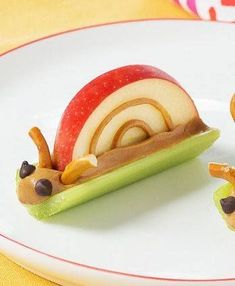 two small figurines are sitting on a plate with an apple and snail in the middle