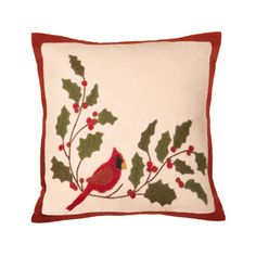 a red bird sitting on top of a pillow with holly leaves and berries around it