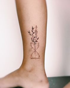 a tattoo on the leg of a woman with a plant in a hour glass vase