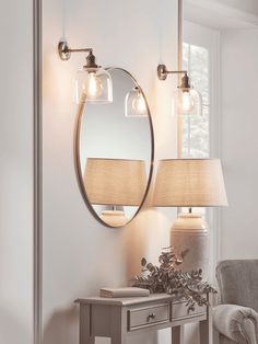 a mirror and two lamps on a wall next to a table with a chair in front of it