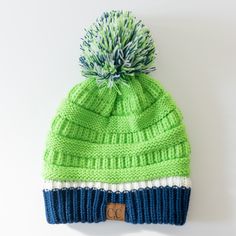 a green and blue knitted hat with a pom - pom on top