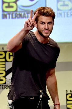 a man making the peace sign while standing in front of a microphone at a comic convention