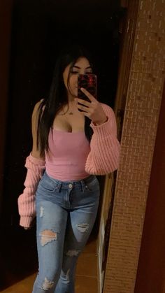 a woman taking a selfie with her cell phone in front of a mirror wearing ripped jeans and pink sweater