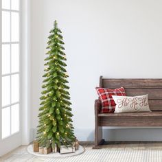 a small christmas tree sitting next to a wooden bench in a room with white walls