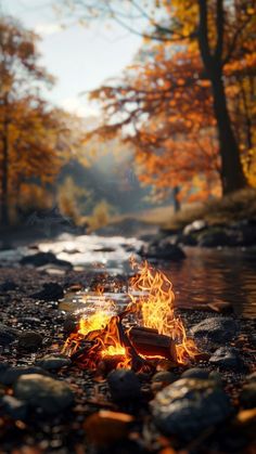 a campfire in the middle of a stream surrounded by rocks and trees with yellow leaves