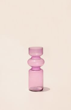 a pink glass vase sitting on top of a white table next to a light colored wall