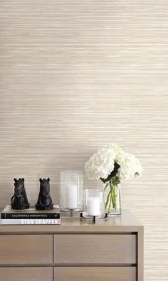 two vases with white flowers on top of a wooden dresser in front of a wall