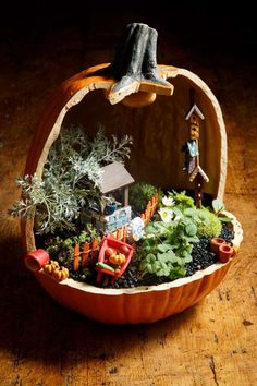 a pumpkin shaped planter filled with lots of plants and miniature people on top of it