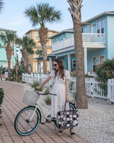 a woman is standing next to her bike on the sidewalk with palm trees in the background