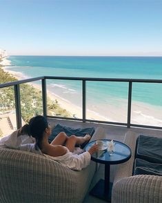 a woman sitting on top of a couch next to a table near the ocean and beach