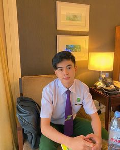 a young man sitting on a couch wearing a tie and holding a book in his lap