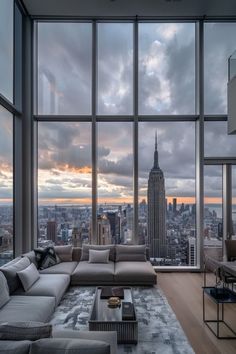 a living room filled with furniture and large windows overlooking the cityscape at sunset