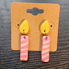 the pink and yellow earrings are hanging from the hooks on the wooden table next to it