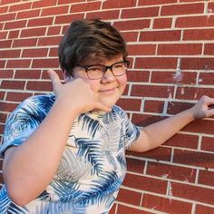 a young boy standing in front of a brick wall with his hand up to the side