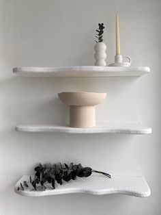 two white shelves with vases and candles on them, one shelf has black flowers in it