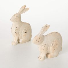 two ceramic rabbits sitting next to each other on a white surface with black speckles