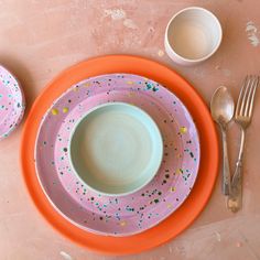 an orange and pink plate with sprinkles on it next to two white bowls