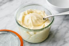 a spoon in a jar filled with whipped cream on a marble counter top next to a white cup