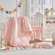 a baby's room with a crib, dresser and bedding in pastel pink