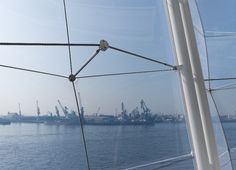 the view from inside a sailboat looking out at ships in the water and cranes