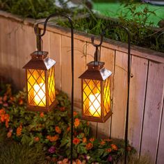 two lights that are next to each other in the grass near flowers and bushes on a fence