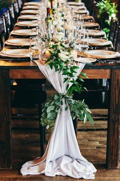 a long table is set with place settings and greenery for an elegant dinner party