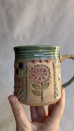 a hand holding a coffee mug with a flower painted on the outside and inside it