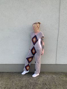 a woman leaning against a wall with her back turned to the camera, wearing a patterned jumpsuit and white sneakers