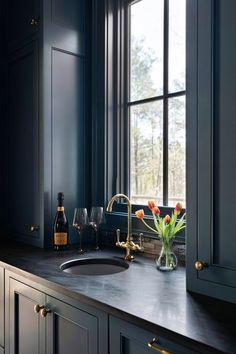 a kitchen with dark blue cabinets and marble counter tops, gold faucets and wine glasses on the window sill