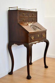 an antique writing desk with drawers and brass accents on the top, against a white wall