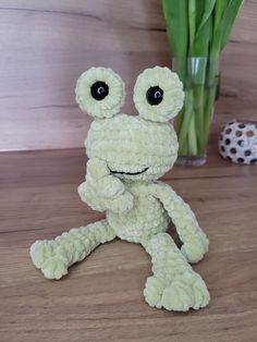 a stuffed frog sitting on top of a wooden table next to a vase with flowers