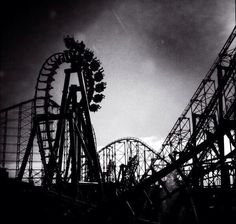 an amusement park ride in black and white with the sun shining through the dark clouds