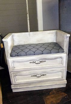 a white dresser with a gray cushion sitting on it's top shelf and bottom drawer