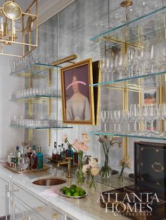 a kitchen counter topped with lots of glass shelves filled with wine glasses and flowers next to a painting