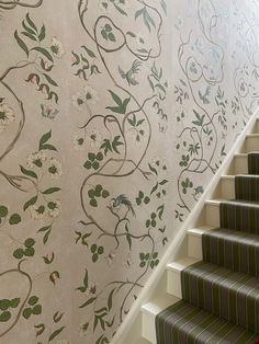 the stairs are lined with floral wallpaper and green carpeted stair treads that lead up to the second floor