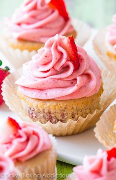 some cupcakes with pink frosting and strawberries on top are sitting on a plate