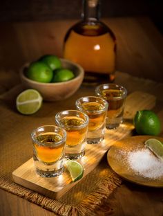 four shot glasses with limes and sugar on a wooden tray next to bowls of limes