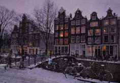 bicycles are parked in front of a row of buildings on a snowy day at night