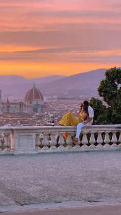 a man and woman kissing on a bridge over looking the city at sunset or sunrise