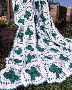 a white crocheted blanket with green shamrocks on it sitting in the grass