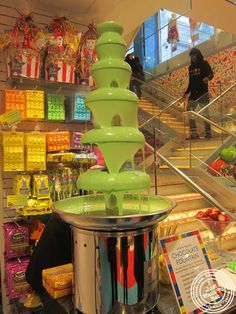 a green water fountain sitting on top of a metal stand in front of a store