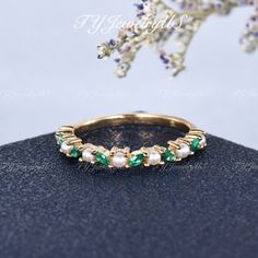 a gold ring with green and white stones on it, sitting next to a branch