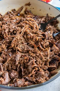 shredded meat in a skillet with tongs on the side, ready to be eaten