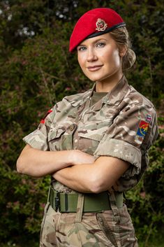 a woman in uniform is standing with her arms crossed and looking at the camera while wearing a red beret