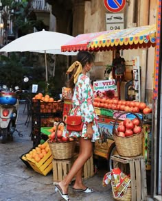 a woman is standing in front of a fruit stand