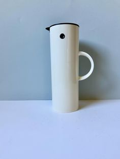 a white and black coffee cup sitting on top of a table next to a wall