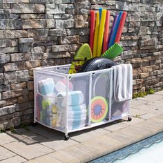 an outdoor storage bin with toys in front of a brick wall next to a swimming pool